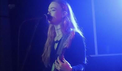 A girl singing on stage playing a guitar