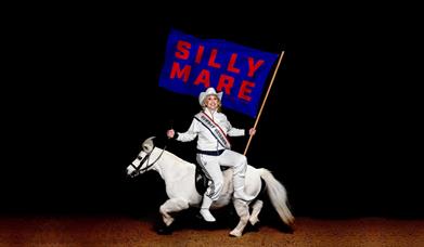 Hayley Ellis sat on a horse holding a flag that reads Silly Mare