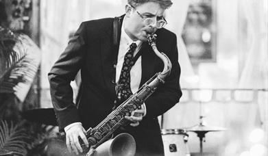 A black and white photograph of a man playing a saxophone at Gin & Juice