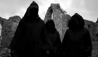 A trio of hooded figures standing in Oystermouth Castle