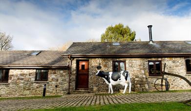 Stone barn with a plastic cow outside.