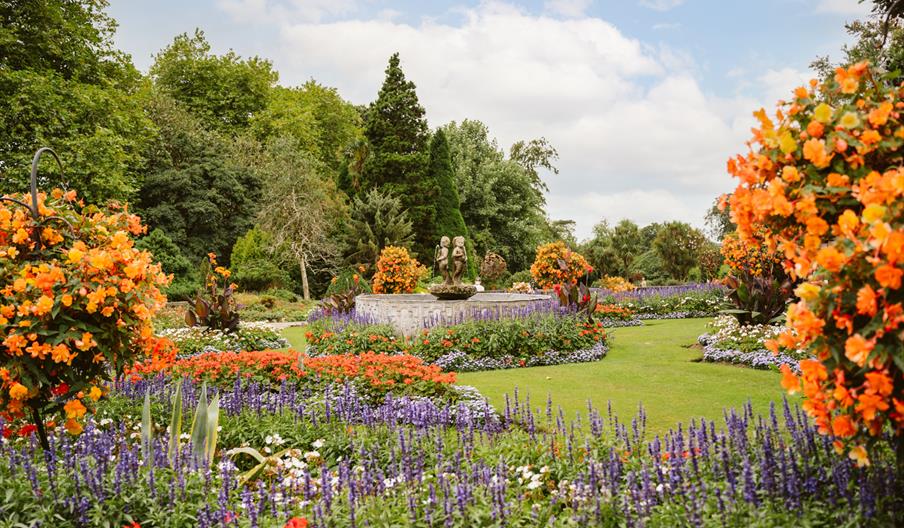 A fountain surrounded by a manicured lawn and colourful flowers.