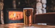 A photo of a pint of Gower Brewery Alcohol on a table in front of a wood burning fire in a pub.