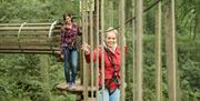 Two women walking across a rope bridge