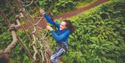 A woman wearing a blue jumper climbing a rope wall.