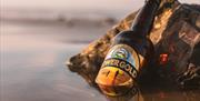 A bottle of Gower Gold leaning on a rock, half covered by the sea.
