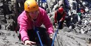 A lady wearing a pink jumper and orange hat taking part of the rock climbing activity available from Gower Adventures.